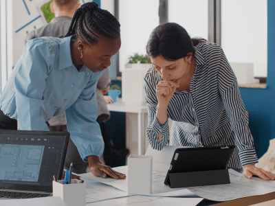 Close up of diverse women analyzing blueprints plan with digital tablet, doing teamwork for project. Architects working on construction layout and structure for urban development.