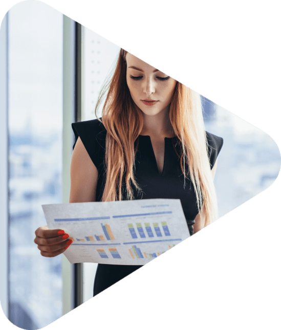 Female financial analyst holding papers studying documents standing against window with city view.