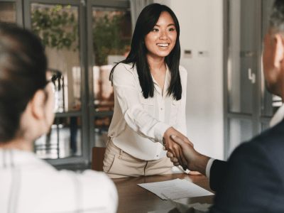 Business, career and placement concept - image from back of two employers sitting in office and shaking hand of young asian woman after successful negotiations or interview