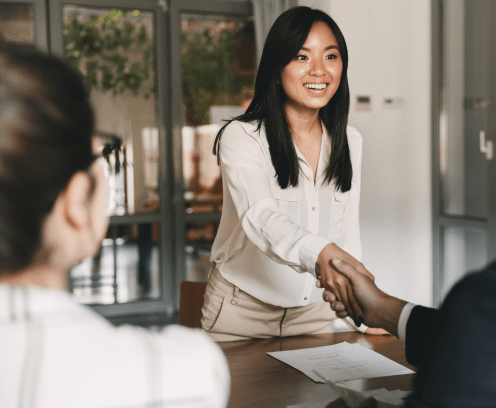 Business, career and placement concept - image from back of two employers sitting in office and shaking hand of young asian woman after successful negotiations or interview