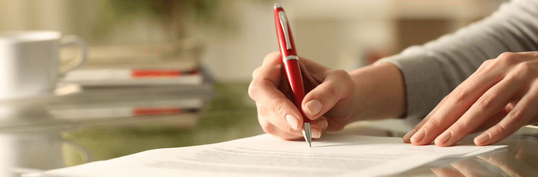 Close up of woman hands signing document with pen on a desk at home