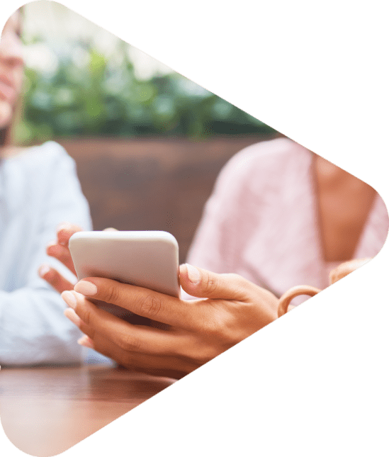 Portrait of two young women enjoying coffee at cafe table and chatting, focus on elegant female hand holding smartphone