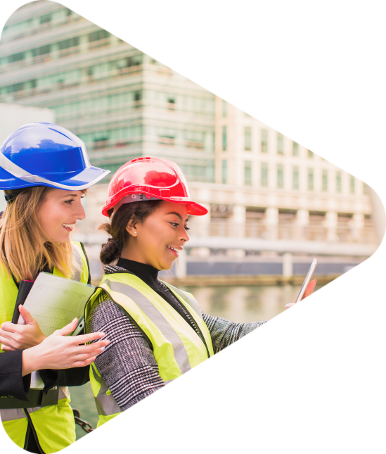 Two young women architects stand together, one of them keeps the folder with a new project, another keeps the tablet and they look at it, outdoors